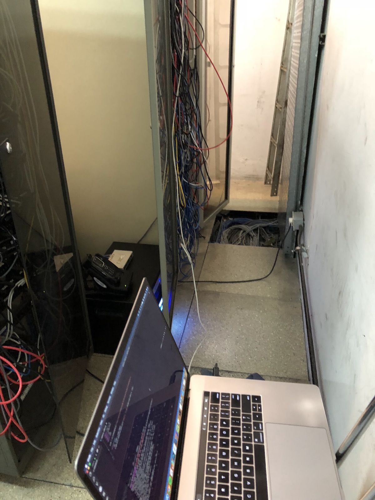 A cramped server room with cable trays overhead and a laptop open on the floor.